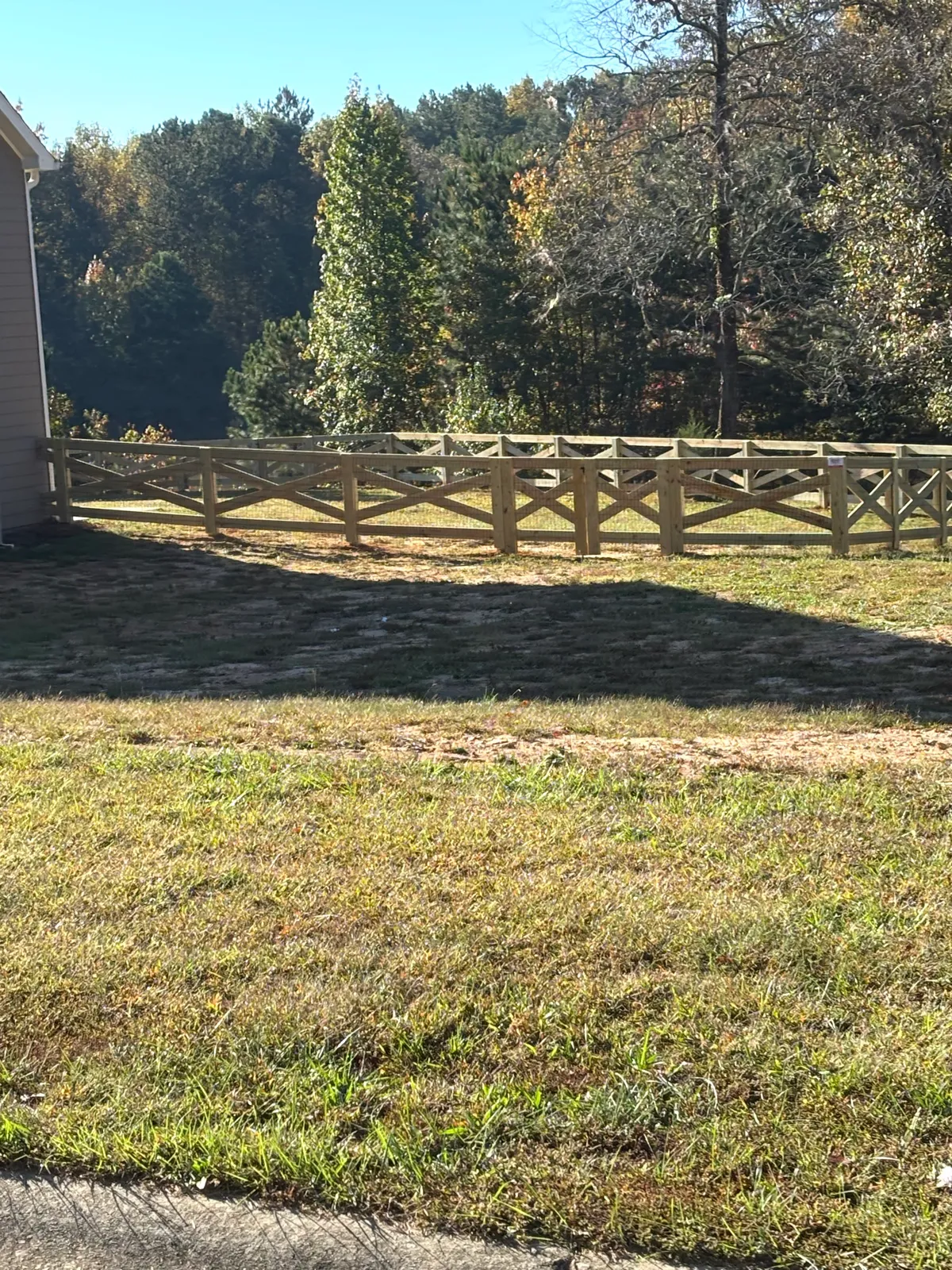 Five-foot open wood crossbuck equestrian fence running along grass lawn in Cumming GA