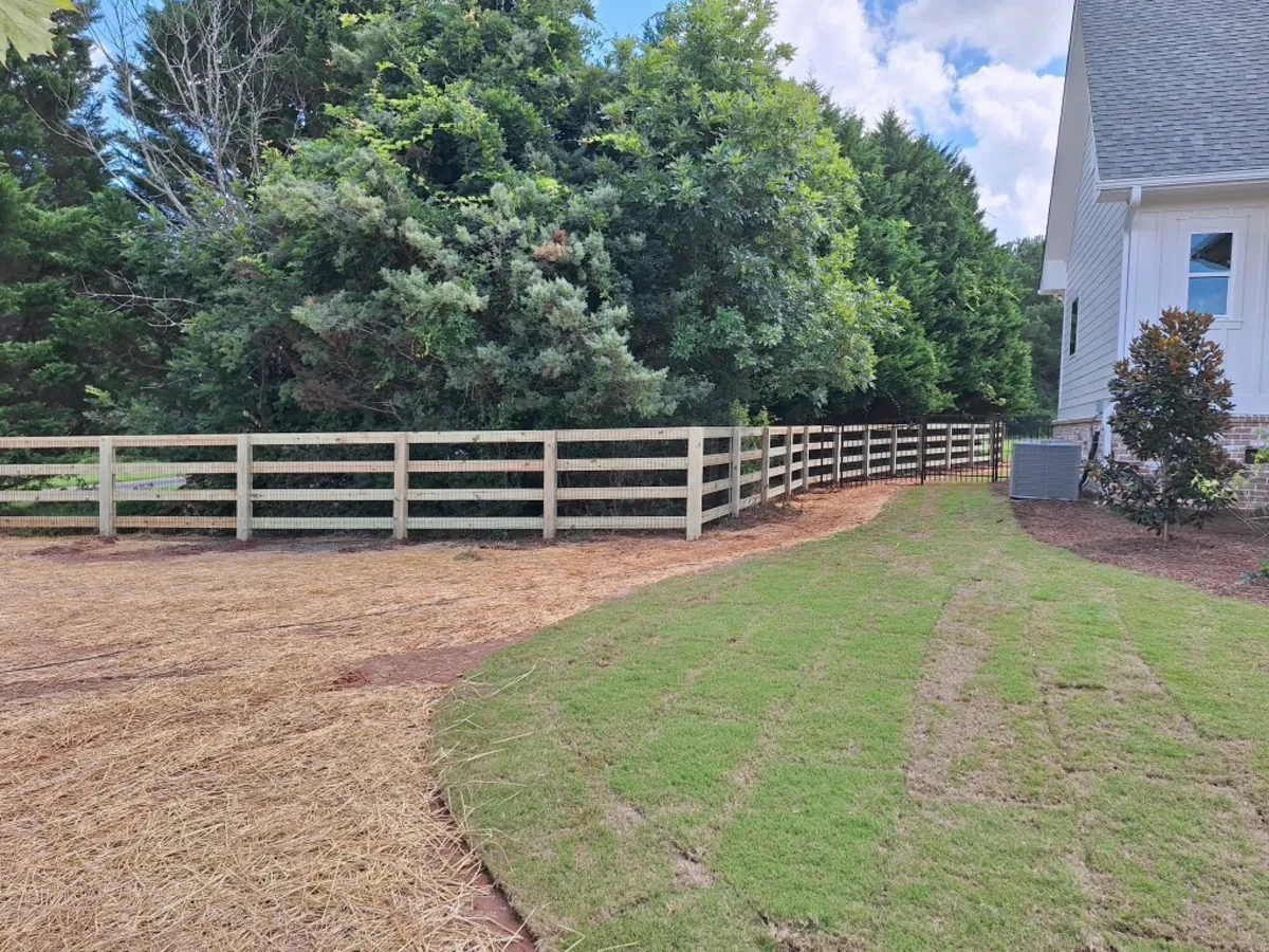 Four-board wood agricultural perimeter fence stretching across rural property in Dawsonville