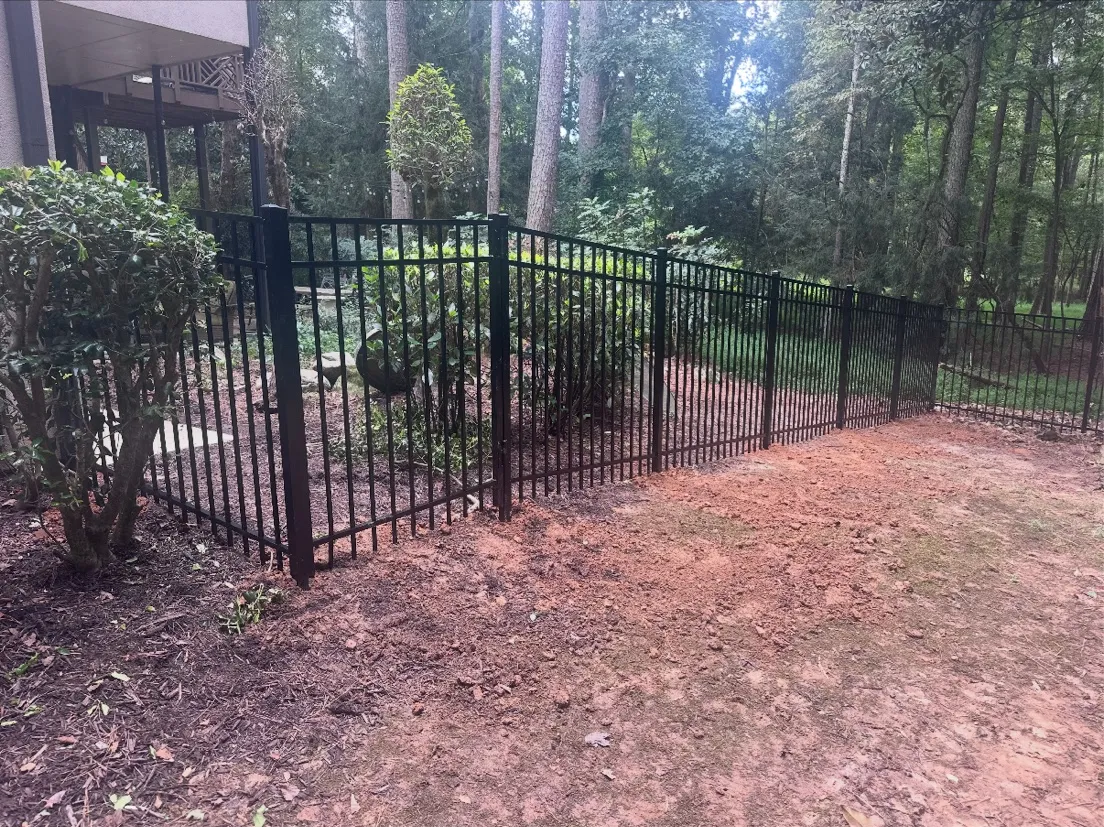 Black ornamental aluminum fence running along wooded tree boundary in Johns Creek